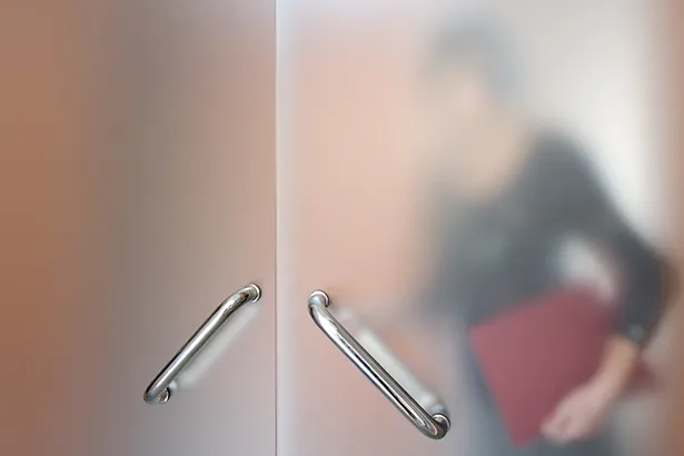 Opaque glass door obscures details of woman holding a folder.