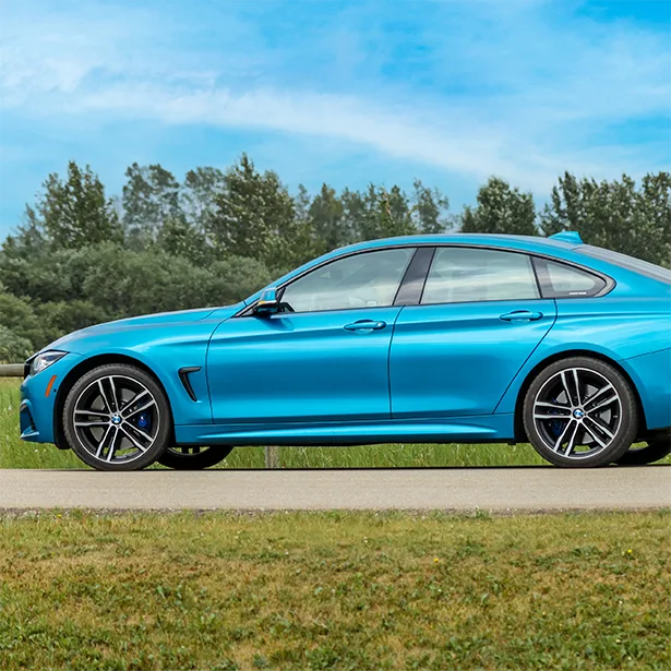 A blue car with 3M auto tint is parked next to a pasture with trees in the background.