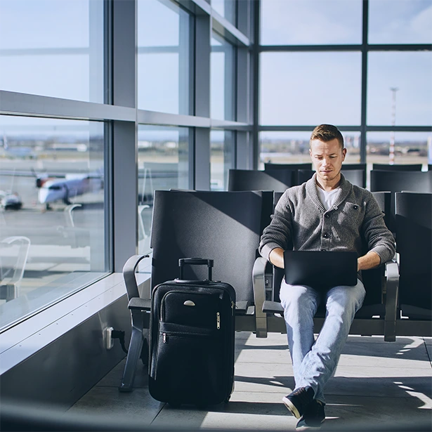 A man sits comfortably in the sunlight at an airport while working on his laptop.