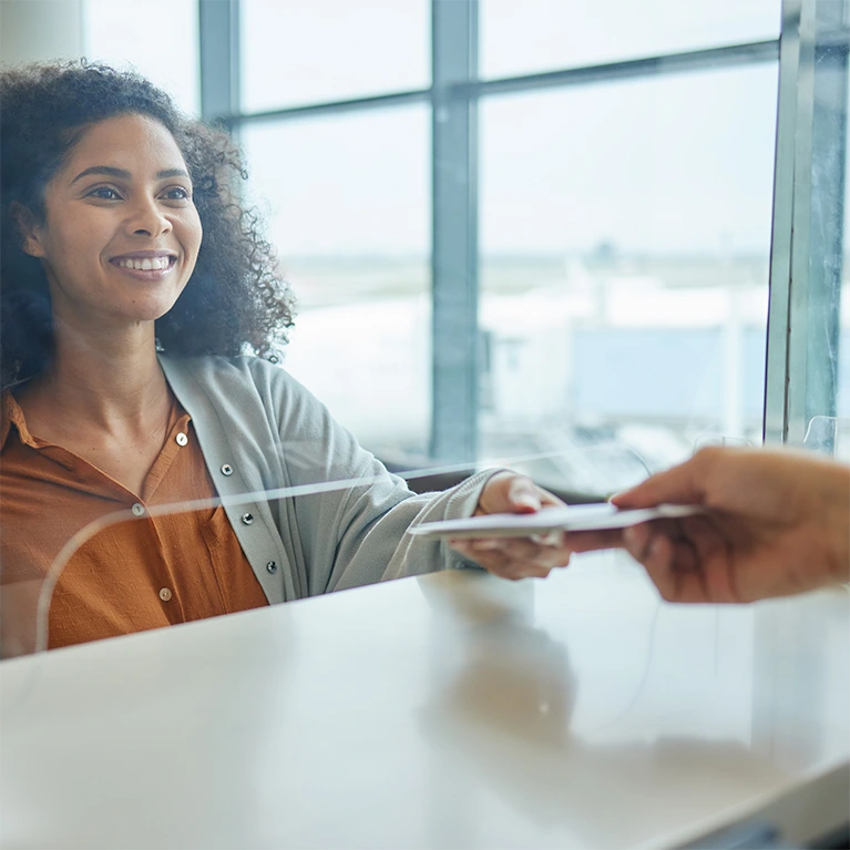 A woman hands over her ticket information through a security window at an airport.