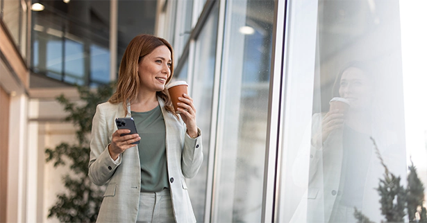 A woman enjoys the office window view while drinking coffee.
